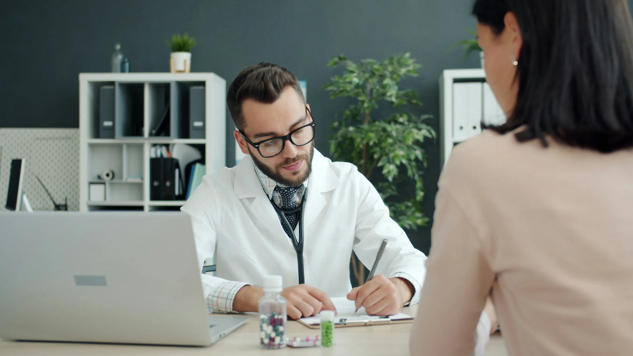 A doctor taking notes while talking with a patient in a consultation room